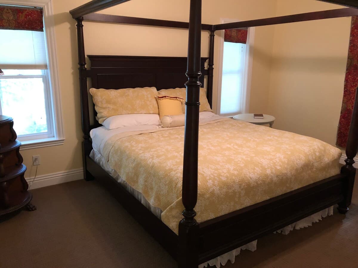 Dark wood four-poster bed with soft yellow bedding